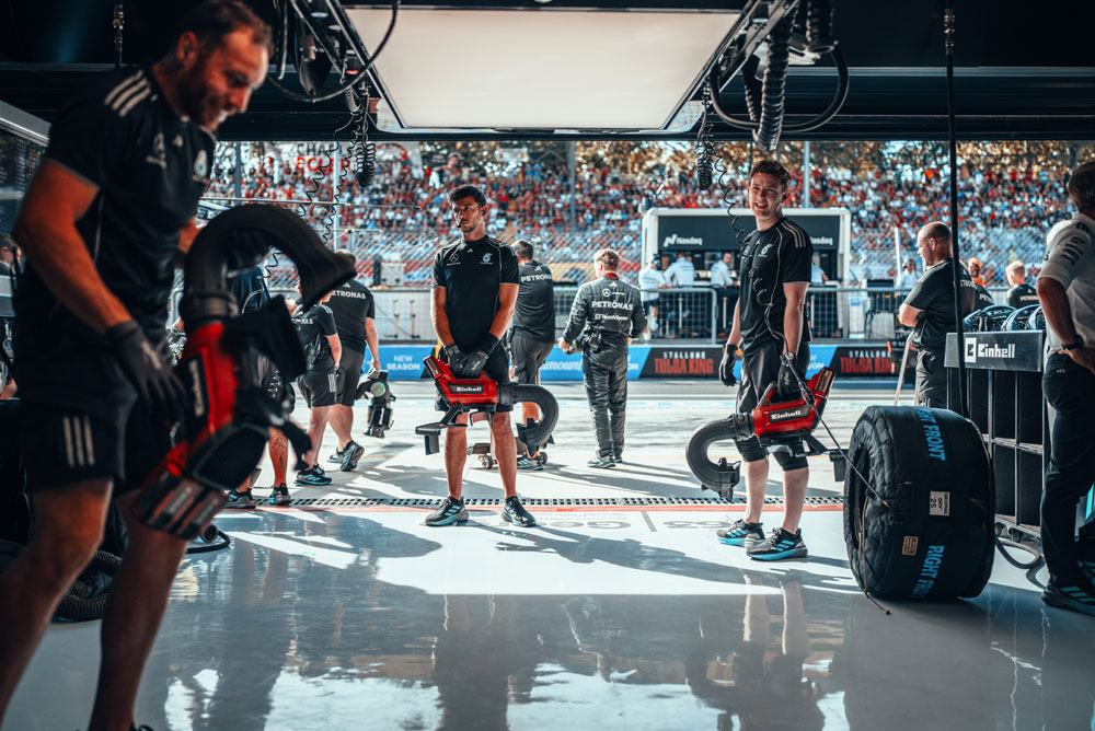 Monteurs van het Mercedes-AMG PETRONAS Formula One Team bereiden zich in de garage voor met snoerloze blazers van Einhell voor een pitstop. Op de achtergrond zijn de tribunes gevuld met fans.