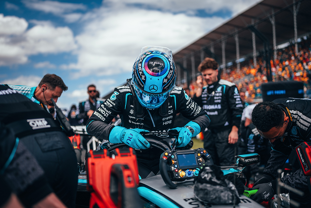 Formule 1-coureur zit in de auto omringd door het team op de startgrid.