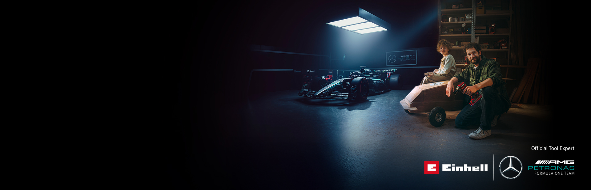 Een vader en kind in een werkplaats met een zelfgemaakte zeepkistauto. Op de achtergrond een Mercedes-AMG PETRONAS Formule 1-wagen en gereedschap van Einhell.