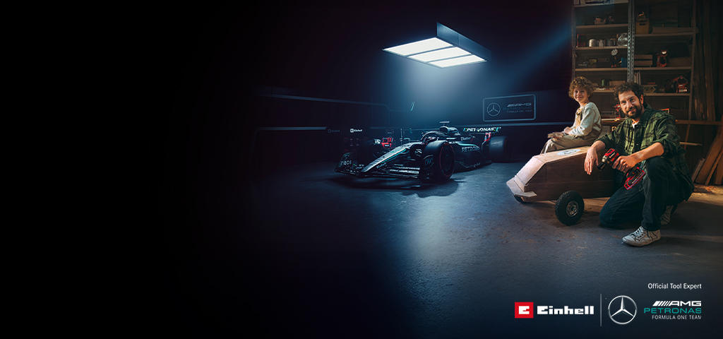 Een vader en kind in een werkplaats met een zelfgemaakte zeepkistauto. Op de achtergrond een Mercedes-AMG PETRONAS Formule 1-wagen en gereedschap van Einhell.