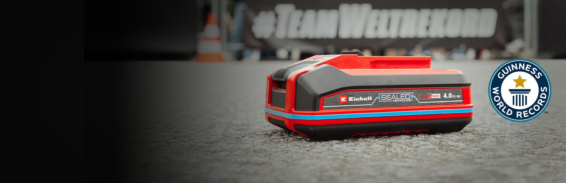 Einhell Power X-Change 4.0 Ah SEALED Accu ligt op het asfalt, met rechts het logo ‘Recordhouder’ van Guinness World Records.