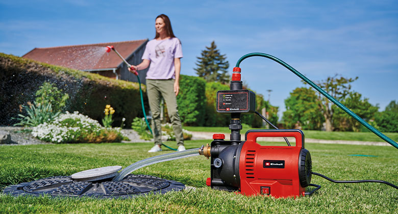 Achter: vrouw die bloemen in de tuin water geeft; voor: waterpomp pompt water.