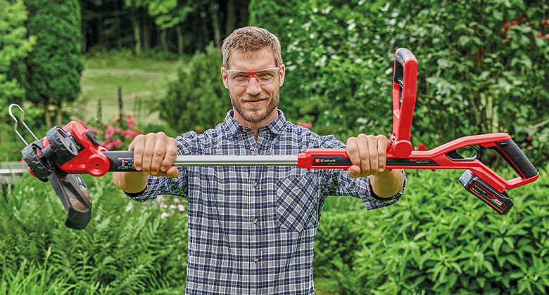 Een man houdt een Einhell-trimmer vast in een tuin.