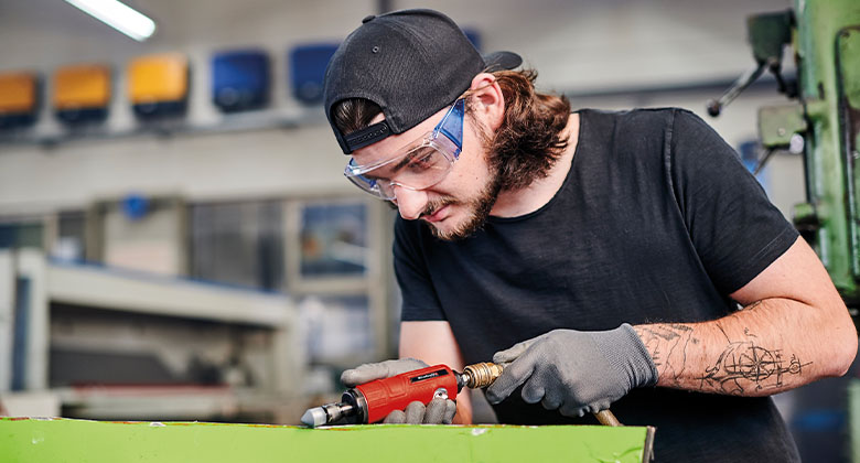 Een man schuurt hout met een pneumatische schuurmachine.