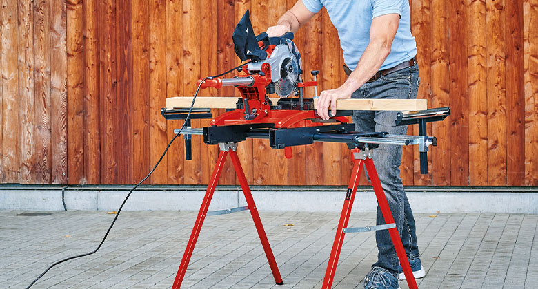 Een man zaagt hout met een trekzaag verstekzaag op een basisframe.